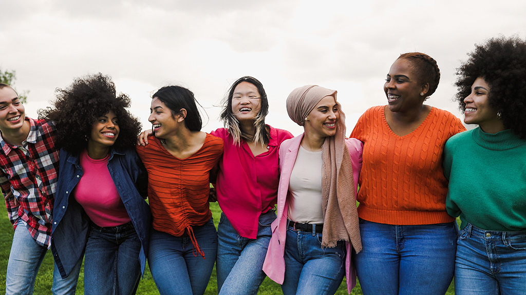A diverse group of women gather together, linking arms and smiling.