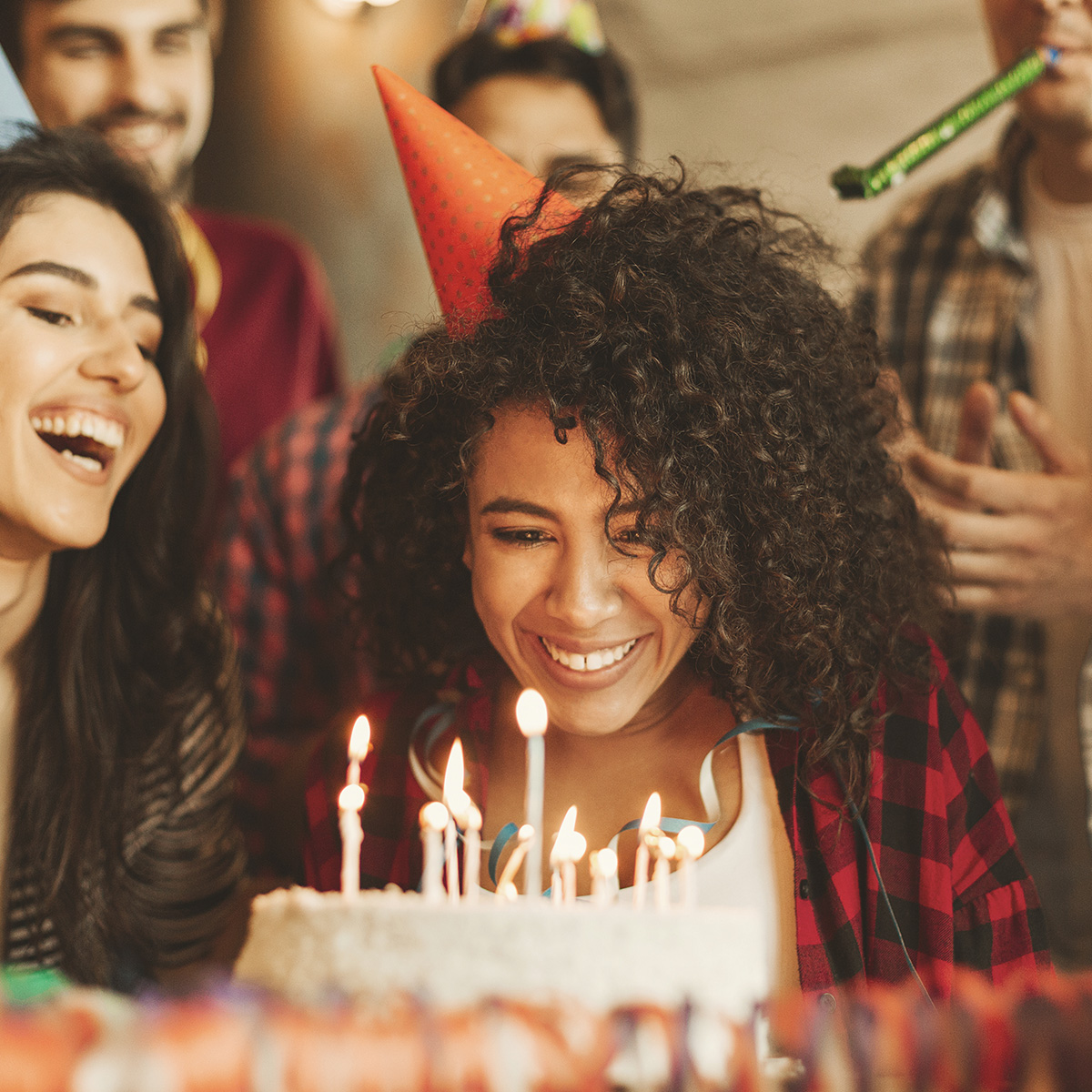 A group of diverse young adults gather around an African American young woman who is about to blow out the candles on her birthday cake