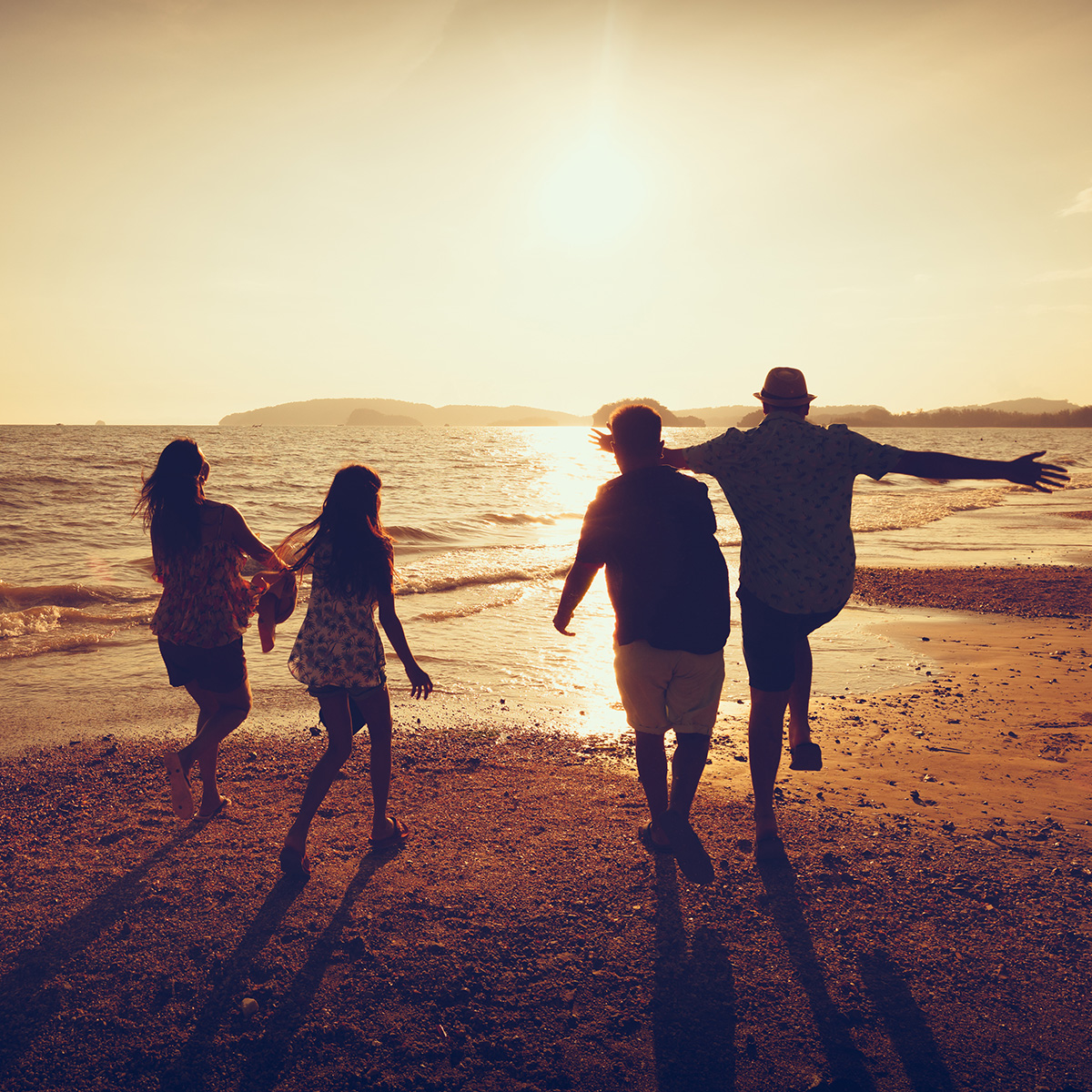family dancing together on a beach while the sun sets