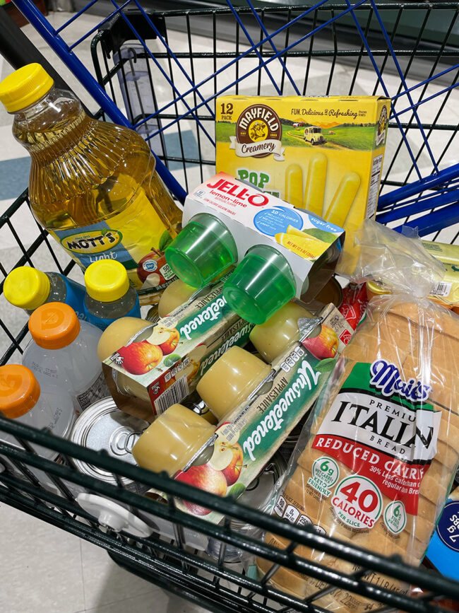 A shopping cart full of colonoscopy prep foods, including applesauce and Jello.