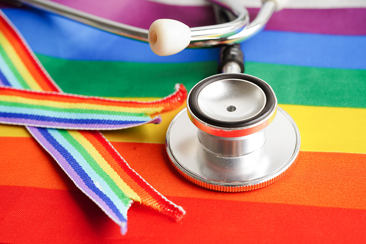 A stethoscope and rainbow ribbon sitting atop a Pride flag.
