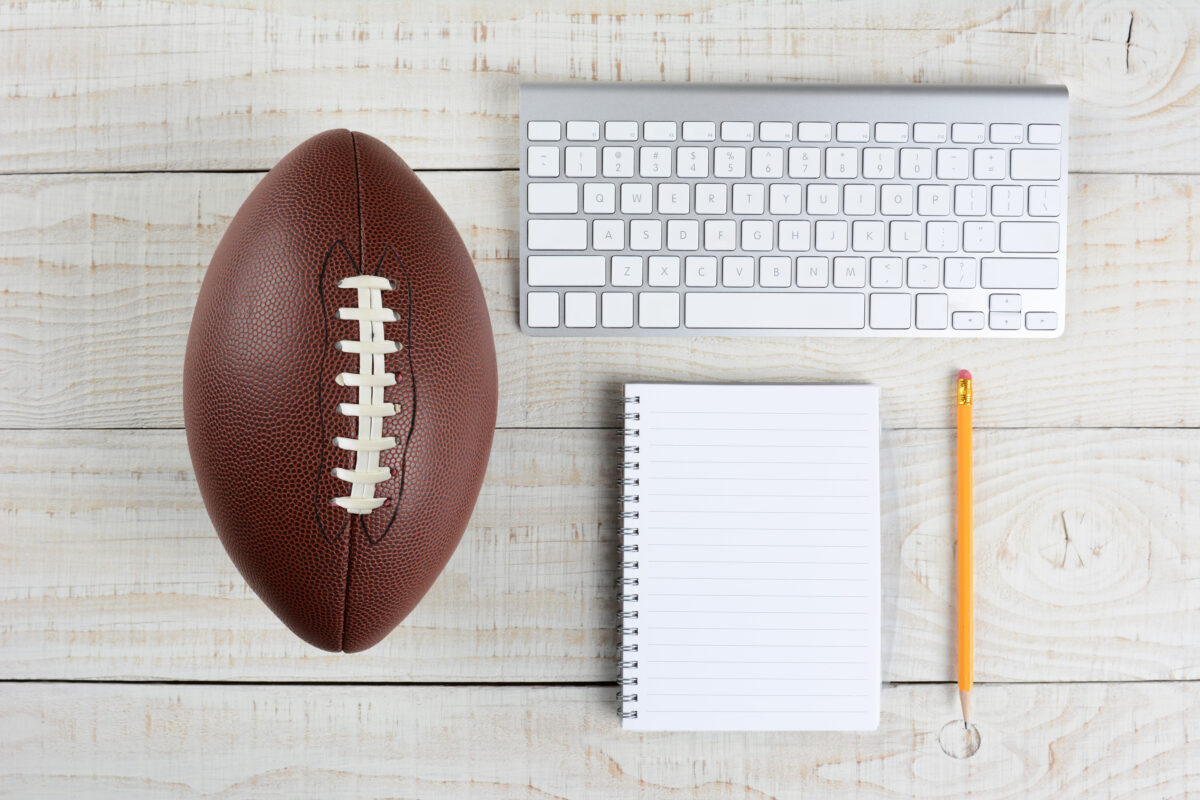 A computer keyboard, pad and pencil and an American style football on a white wood table in a home office.